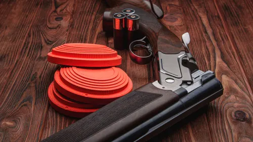 Italian shotgun resting beside a stack of orange clay targets